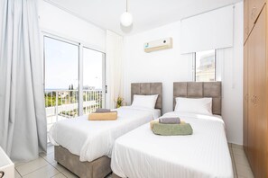 A hotel room with two beds, a balcony, a large window, and an air conditioning unit. - Protaras View 2 - Fig tree Bay Central Protaras (Paralimni)