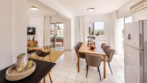 Een moderne keuken met een koelkast, een eethoek met een tafel en stoelen, en een televisie op de achtergrond.