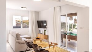 Een moderne woonkamer met een bank, stoelen, een salontafel met fruit, een televisie en een pooltafel.