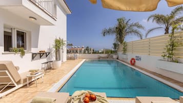 A swimming pool with lounge chairs and a table, surrounded by a white building with a balcony.