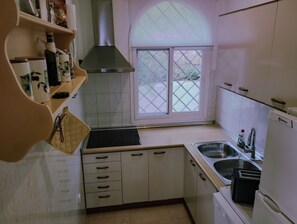 Ett kök med vita skåp, en rostfri köksfläkt, ett fönster med utsikt och en diskho.