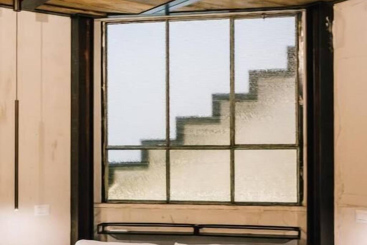 Una habitación con una cama, un ventanal con vista a un edificio y un techo de madera.