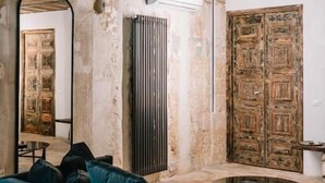 Una stanza con soffitto in legno, un tavolo rotondo, un divano con cuscini, uno specchio e una porta in legno.