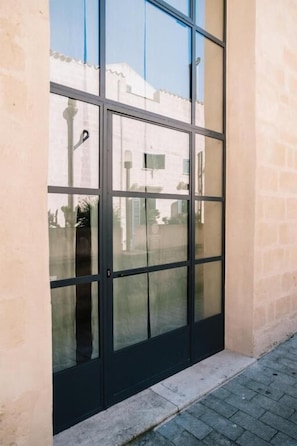 A building facade with a large glass door, a brick wall, and a paved ground. - Il Granile Contemporary Loft  (Matera)