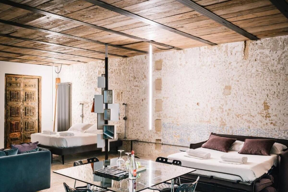 Una habitación con una cama, un sofá, una mesa de vidrio con botellas y una pared de piedra.