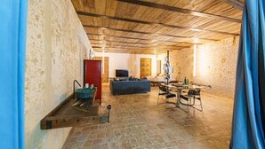 Un interno con parete in pietra, travi in legno a soffitto, un divano, una televisione e una zona pranzo con sedie e tavolo.