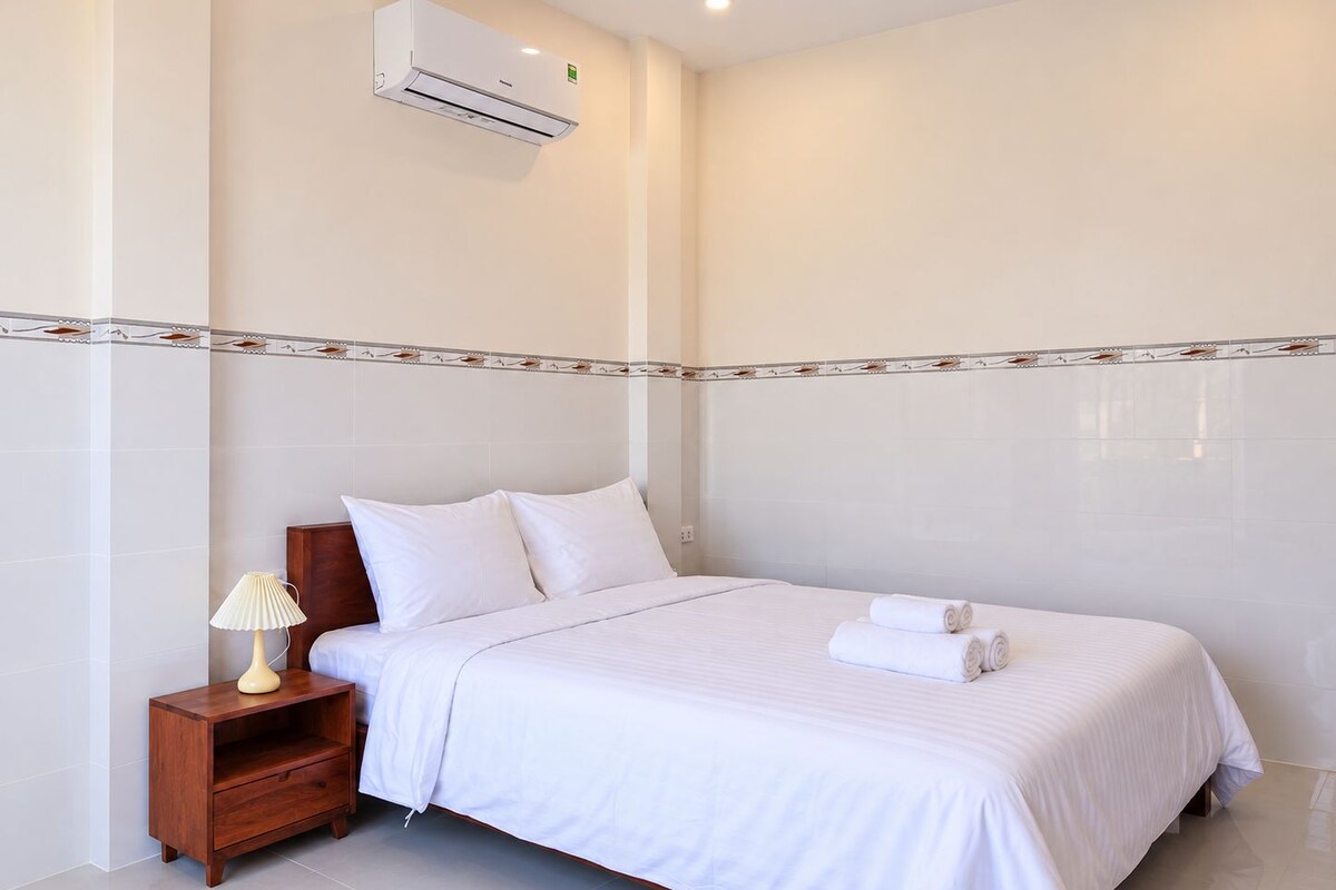 A hotel room with a bed, a nightstand, a lamp, and an air conditioning unit.