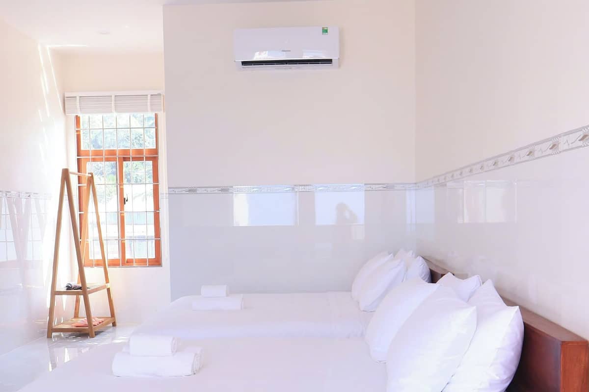 Una cama grande con sábanas blancas, una escalera de madera y un equipo de aire acondicionado en la pared.