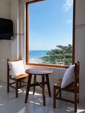 A room with a large window overlooking a beach, two wooden chairs, and a small round table.