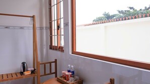 A room with a wooden table, chairs, a window with bars, a shelf with a kettle, and a tray with drinks. - Prospera - Hòn Sơn Beachfront Hotel  (Kien Hai)