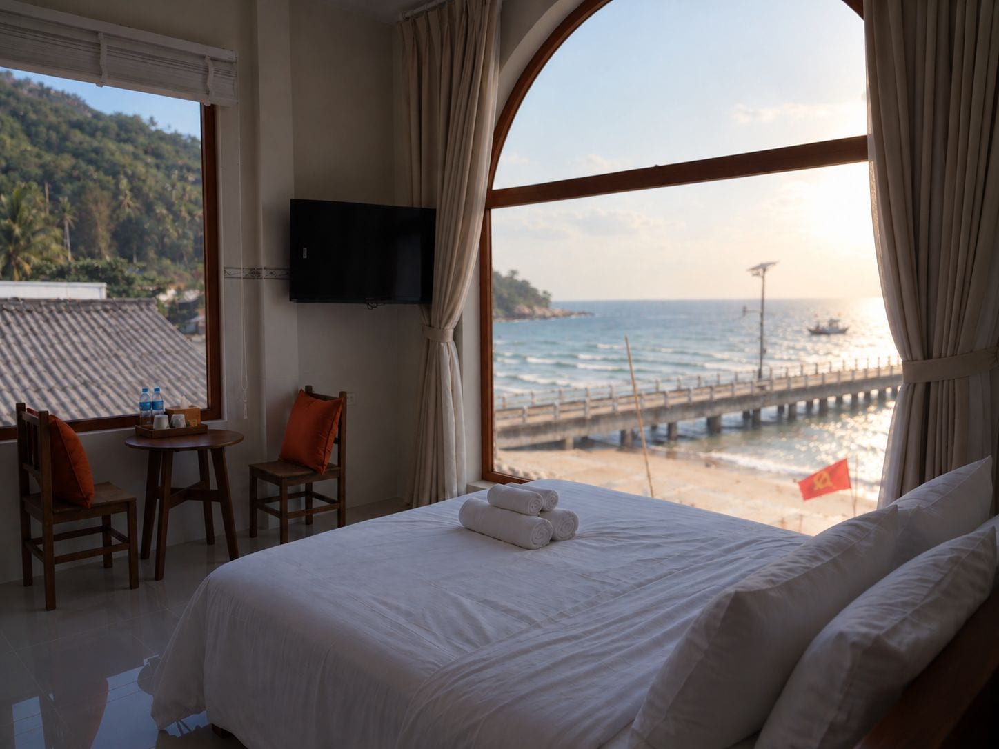 A hotel room with a bed, a TV, a table with chairs, and a view of the sea.