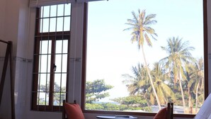 A hotel room with a bed, a small table, two chairs, and a window with a view of palm trees. - Prospera - Hòn Sơn Beachfront Hotel  (Kien Hai)