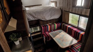 A compact, cabin-style room with a bunk bed, a small kitchenette, and a dining area with striped seating. - 1 Bed Vehicle Luxury Camper -hot Tub, Pets - Willy (Skegness)