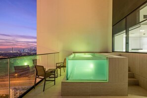 A modern balcony with a glass enclosure, a hot tub, and a view of a city skyline at dusk. - FIRST CLASS | 2BR | Tranquil & Chic Living (JVC)