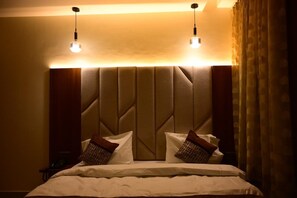 A hotel room with a large bed, a headboard with a geometric pattern, two bedside lamps, and a nightstand with a telephone. - JBS Regency Hotel and Banquet (Haridwar)