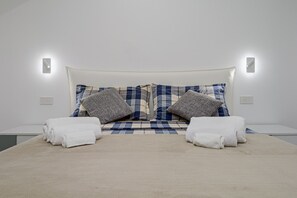 Een bed met een wit hoofdeinde, twee kussens en twee opgevouwen handdoeken.