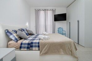 Une chambre à coucher moderne avec un lit, une télévision, une armoire et une chaise.