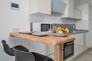 A modern kitchen with white cabinets, a microwave, a sink, and a wooden table with chairs. - 'Pascoli Suite Apartment' with Sea View, Wi-Fi and Air Conditioning (Golfo Aranci)
