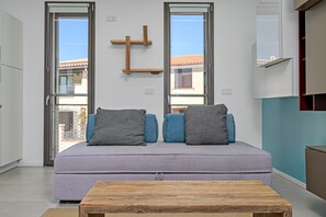 Un salon moderne avec un canapé, des coussins, une table basse en bois et une porte-fenêtre coulissante donnant sur un espace extérieur.