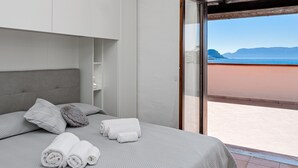 Ein Schlafzimmer mit Bett, Kissen, Handtüchern, einem Kleiderschrank und Blick auf den Strand.