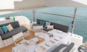 A yacht interior with a dining area, seating, and a view of the water.