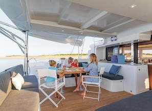 A dining area on a yacht with a table, chairs, and a view of the sea.