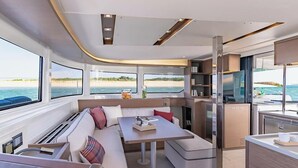 A modern yacht interior with a dining area, seating, and a kitchen.