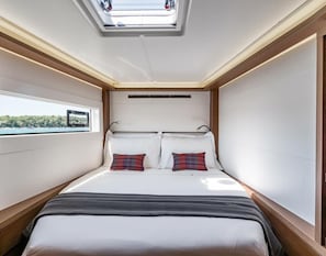 A compact, well-lit bedroom with a skylight, a bed with two pillows, and a window offering a view.