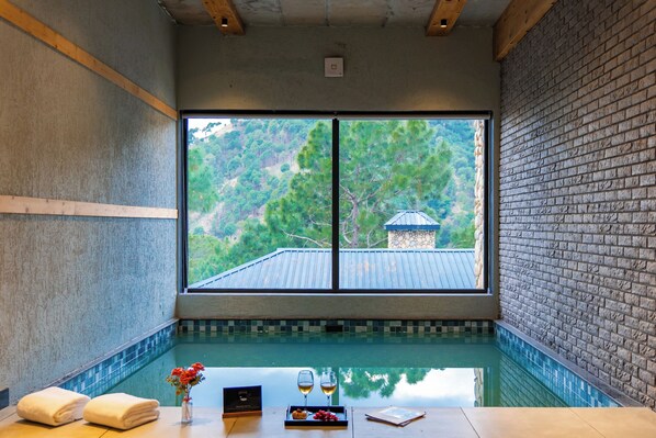 A spa room with a view of a mountain landscape, a pool, and a wooden table with amenities.