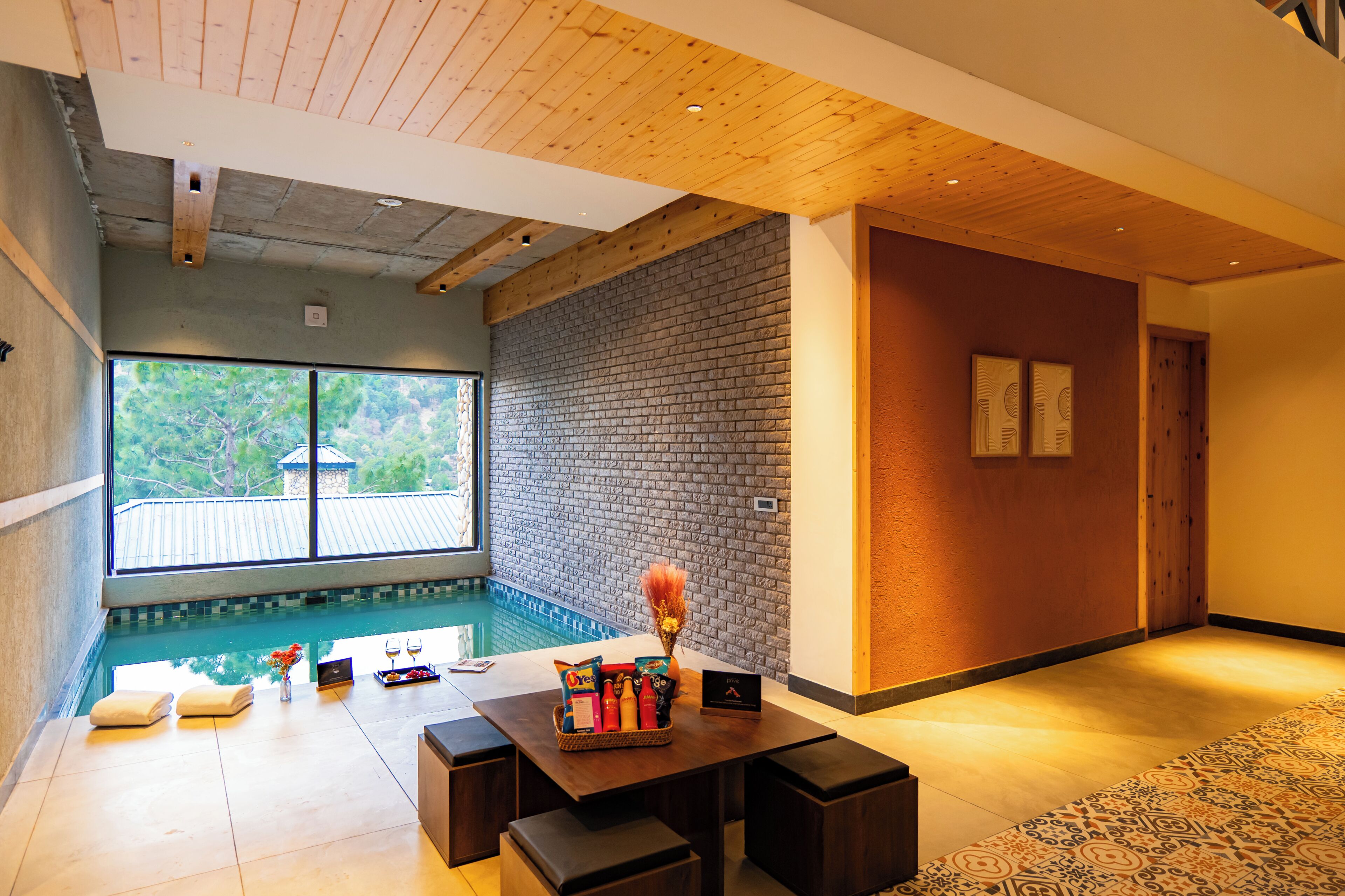 Un área de piscina interior moderna con techo de madera, pared de ladrillo y vistas al exterior.