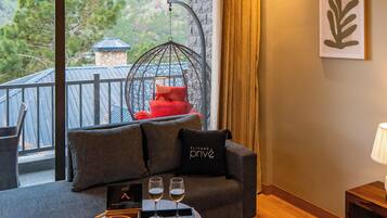 Quarto de hotel com varanda, sofá, cadeira suspensa, cama e mesa de jantar com bandeja de petiscos e copos.