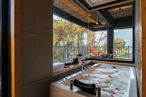 Uma casa de banho moderna com uma banheira grande, uma janela com vista para árvores e teto de madeira.