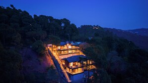Un edificio de varios pisos con una escalera que conduce a la entrada, rodeado de un bosque frondoso.
