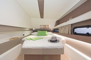 Um espaço interior pequeno e bem iluminado, com uma cama, almofadas, um chapéu e uma janela.