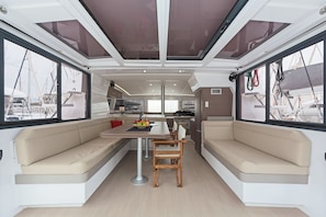 Interior moderno de barco com área de refeições, assentos e cozinha.
