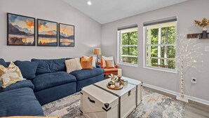 A living room with a blue sofa, a coffee table, and artwork on the wall. - The Blue Jay | New House in the Woods w/ Hot Tub (Harpers Ferry)