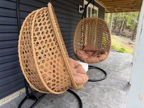 Dos sillones colgantes de mimbre con cojines en un porche.