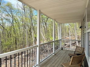 Una terraza de madera con barandilla, sillas de mimbre y vistas a un bosque.