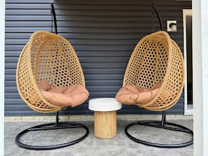 Dos sillas colgantes con cojines, una mesita redonda y un taburete de madera.
