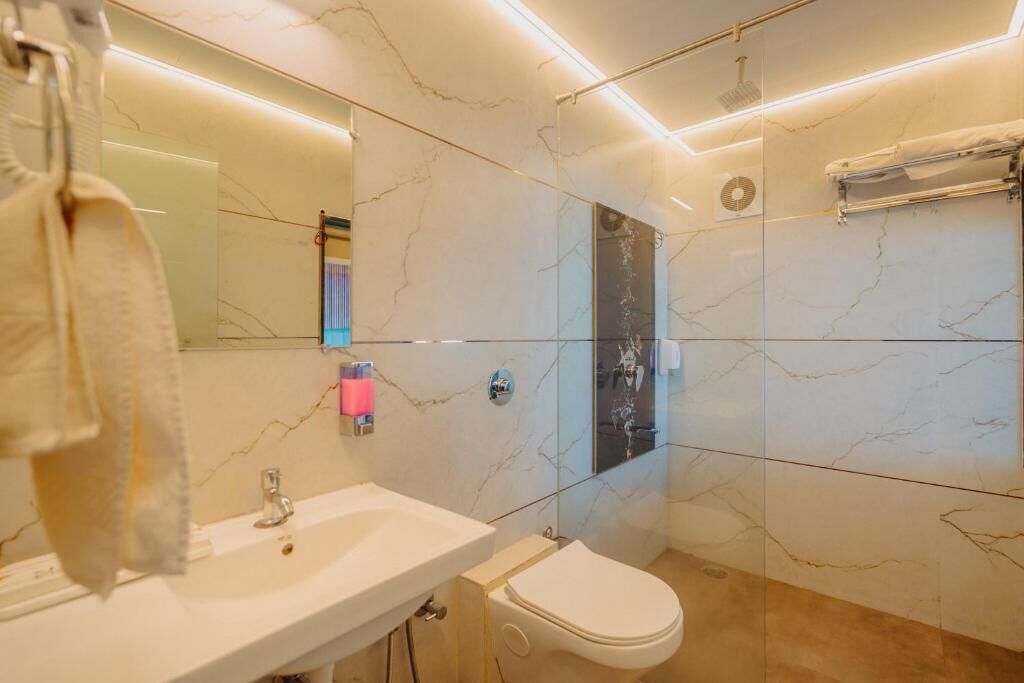 Ein modernes Badezimmer mit Marmorwand, Waschbecken in Weiß, Toilette und einer Duschkabine aus Glas.