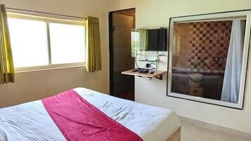 Une chambre d’hôtel avec un lit, une fenêtre avec des rideaux, un téléviseur fixé au mur et une salle de bain visible à travers la fenêtre.
