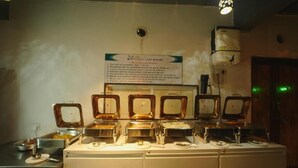 A buffet setup with multiple serving stations, a sign detailing the buffet hours, and a ceiling-mounted air conditioning unit. - Nisarga Lake Resort Tapola (Mahabaleshwar)