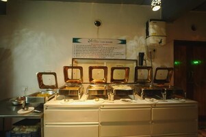 A buffet setup with multiple serving stations, a sign detailing the buffet hours, and a ceiling-mounted air conditioning unit.