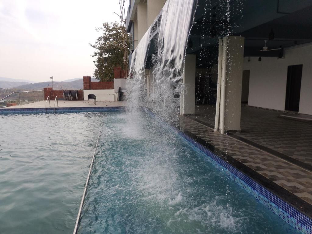 Une piscine agrémentée d’une cascade, un espace salon couvert et une vue sur les montagnes.