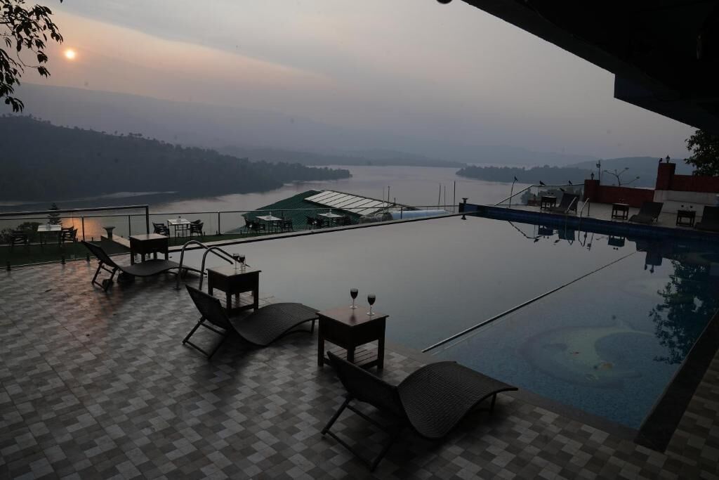 An outdoor infinity pool with lounge chairs and a table, overlooking a body of water and distant hills.