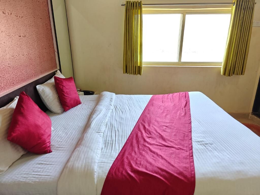 Uma cama com roupa de cama branca e rosa, uma cabeceira e uma janela com cortinas.