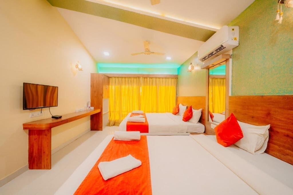 A hotel room with two beds, a TV, a desk, and an air conditioning unit.