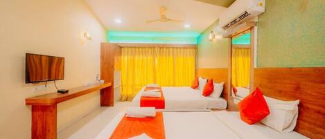A hotel room with two beds, a TV, a desk, and an air conditioning unit.