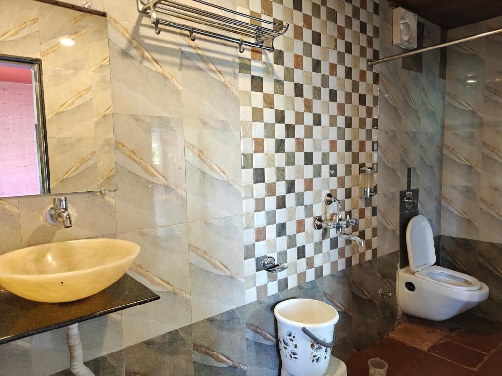A bathroom with a marble sink, a checkered tile wall, a toilet, and a cup on a small table.