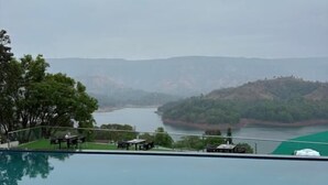 A swimming pool with a view of a river and hills. - Nisarga Lake Resort Tapola (Mahabaleshwar)
